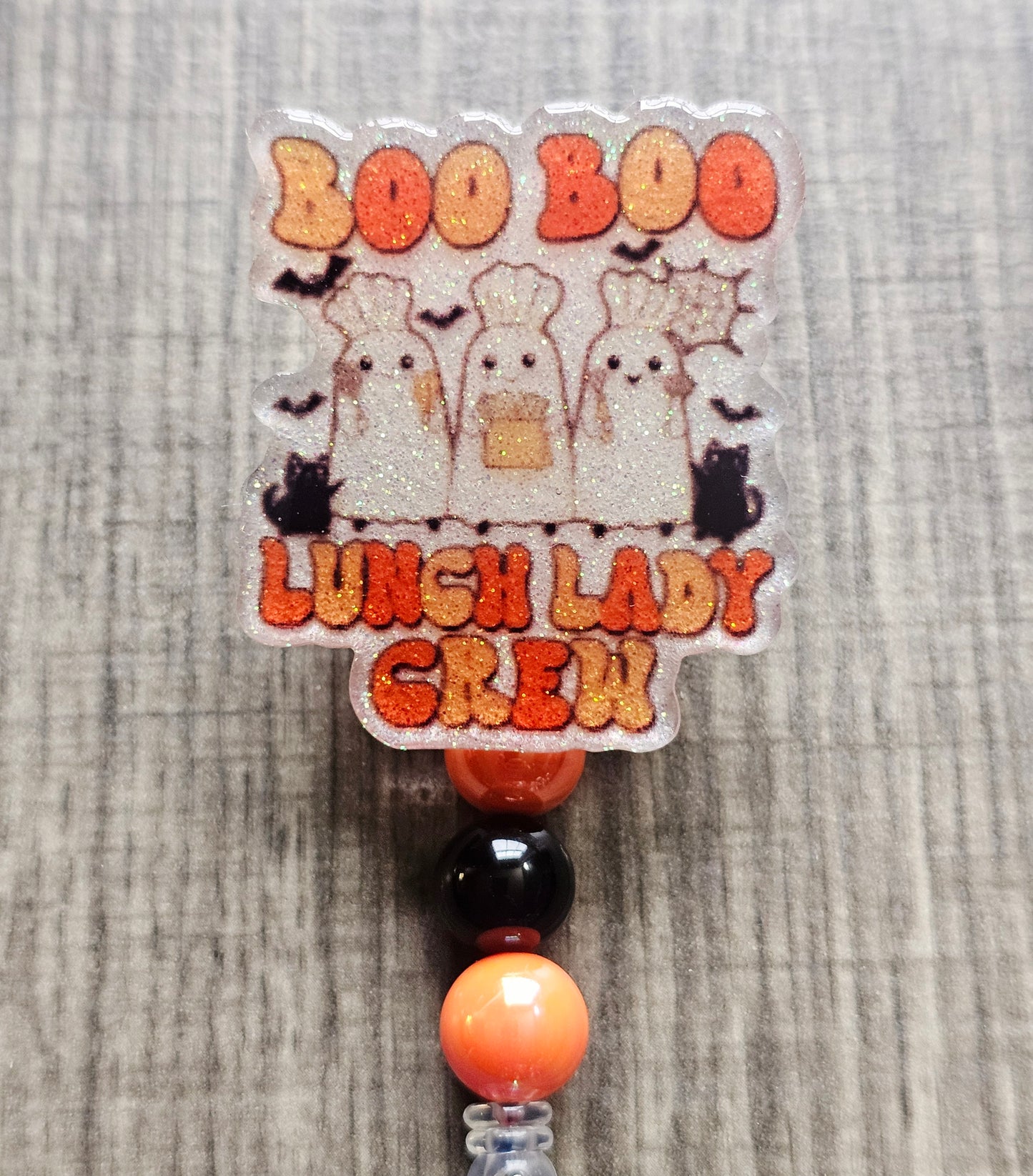 White glitter acrylic badge reel with "Boo Boo Lunch Lady Crew" in a retro Halloween theme, featuring three ghost lunch ladies in chef hats with black cats, bats, and cooking utensils, with matching decorative beads.