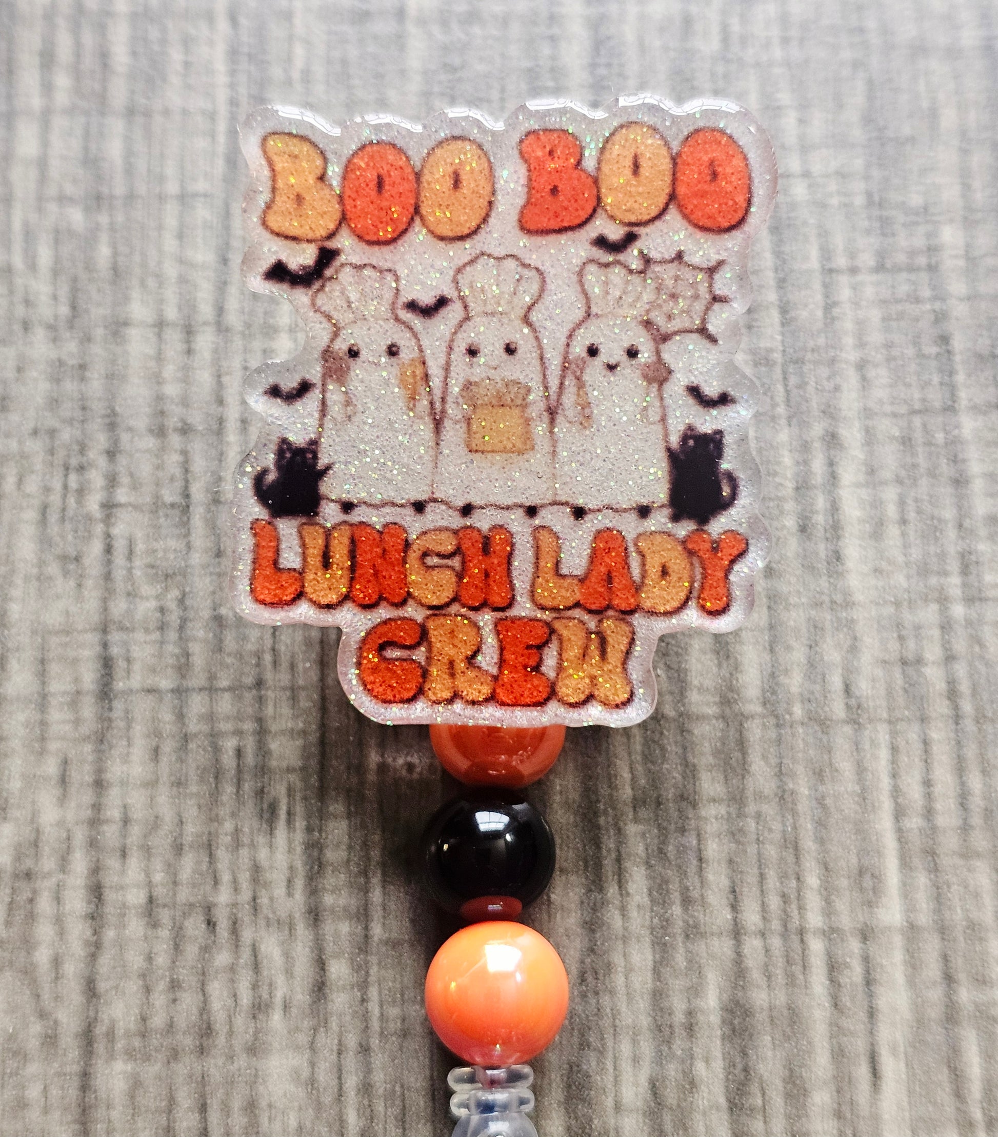White glitter acrylic badge reel with "Boo Boo Lunch Lady Crew" in a retro Halloween theme, featuring three ghost lunch ladies in chef hats with black cats, bats, and cooking utensils, with matching decorative beads.