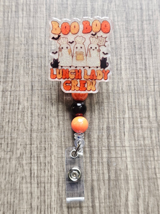 White glitter acrylic badge reel with "Boo Boo Lunch Lady Crew" in a retro Halloween theme, featuring three ghost lunch ladies in chef hats with black cats, bats, and cooking utensils, with matching decorative beads.