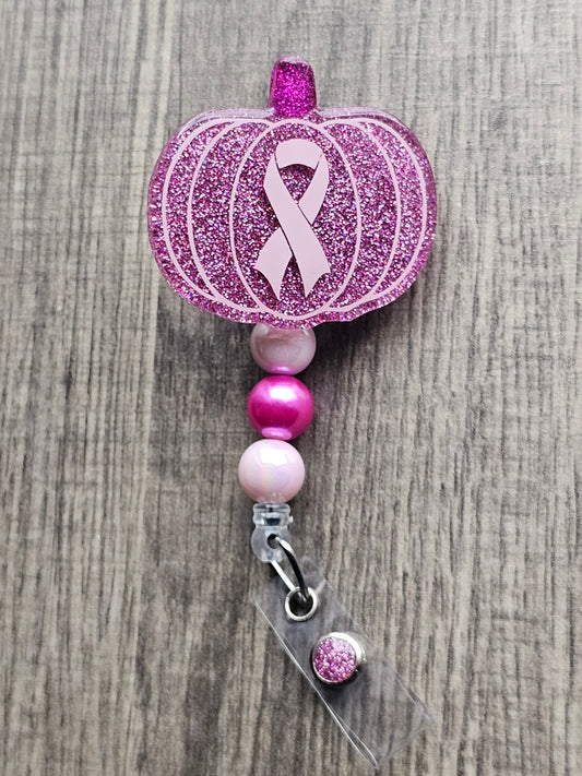 a pink badge reel in the shape of a pumpkin with a breast cancer awareness symbol in the middle