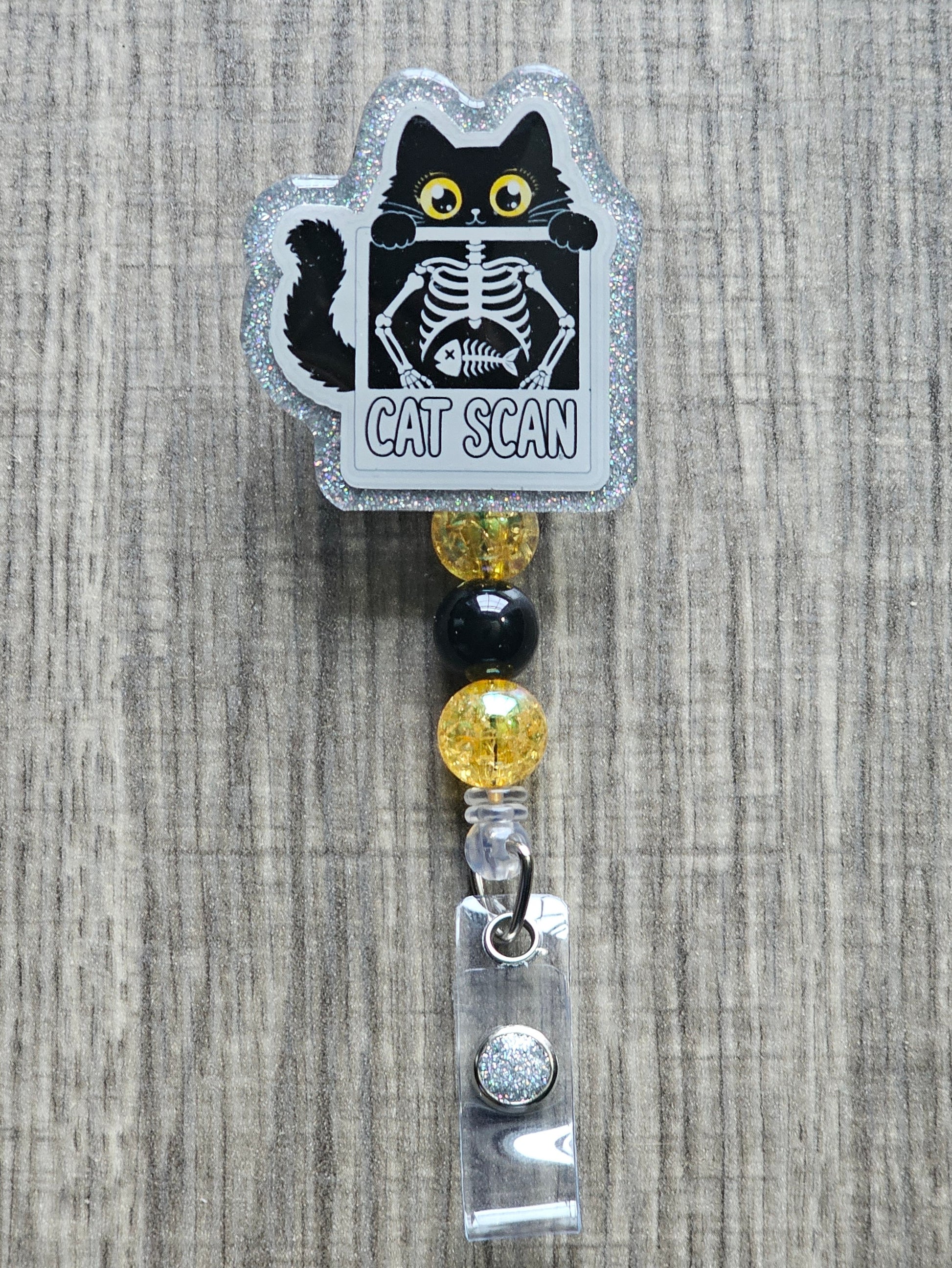 Retractable badge reel with a "Cat Scan" acrylic topper featuring a black cat and its X-ray skeleton, accented with yellow and black beads.
