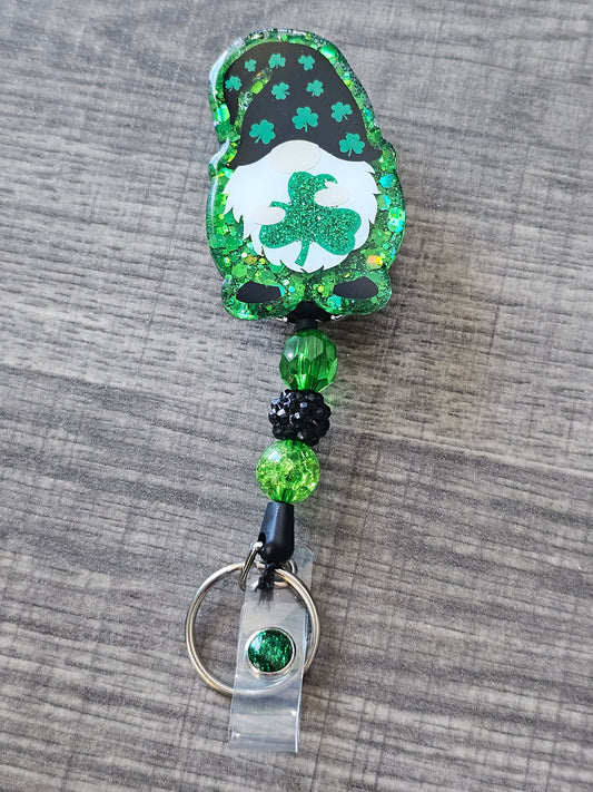 A badge reel featuring an adorable gnome dressed in a festive clover-adorned hat and holding a lucky clover leaf