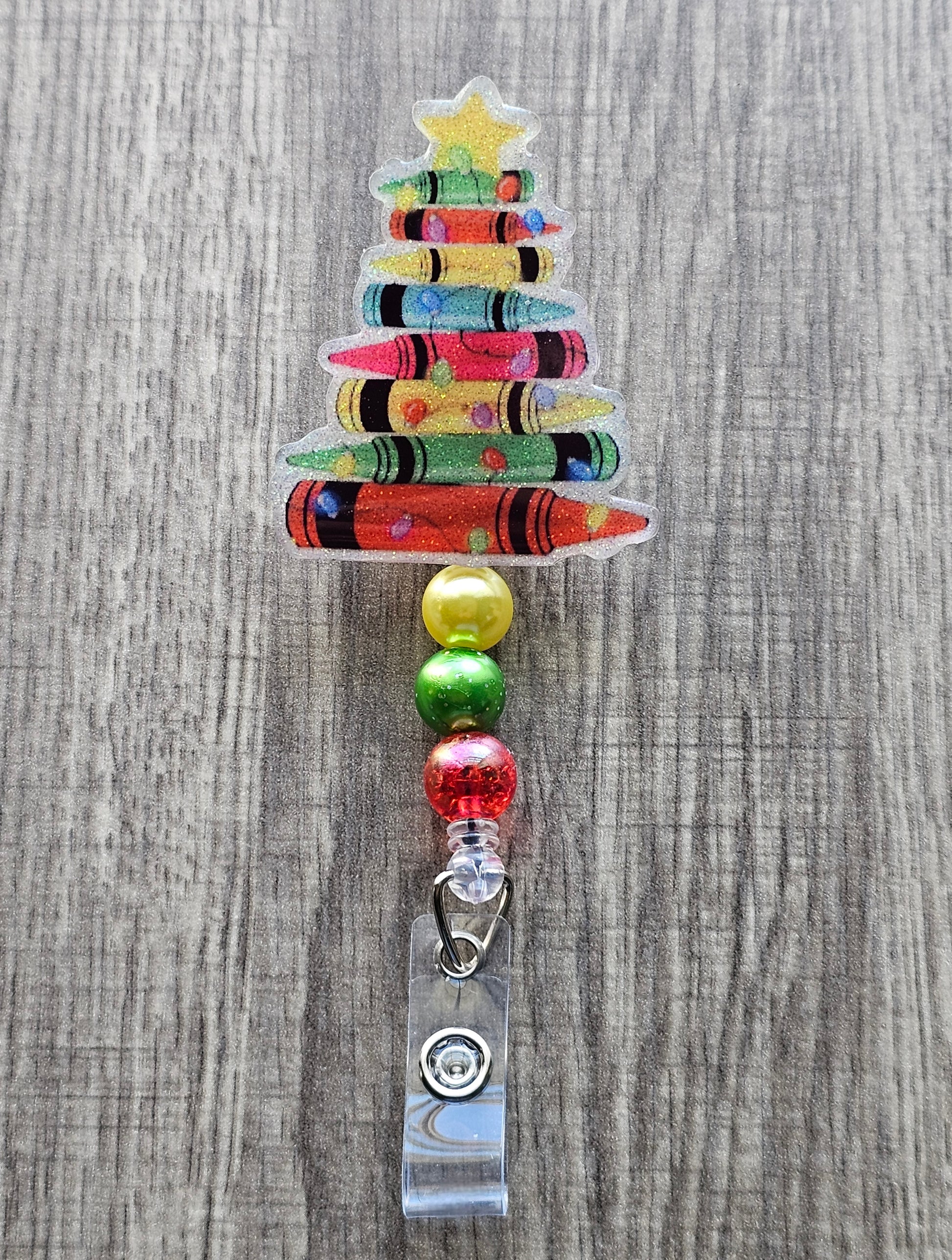 A badge reel featuring a a Christmas tree made from crayons along with a golden star featured at the top of the tree.