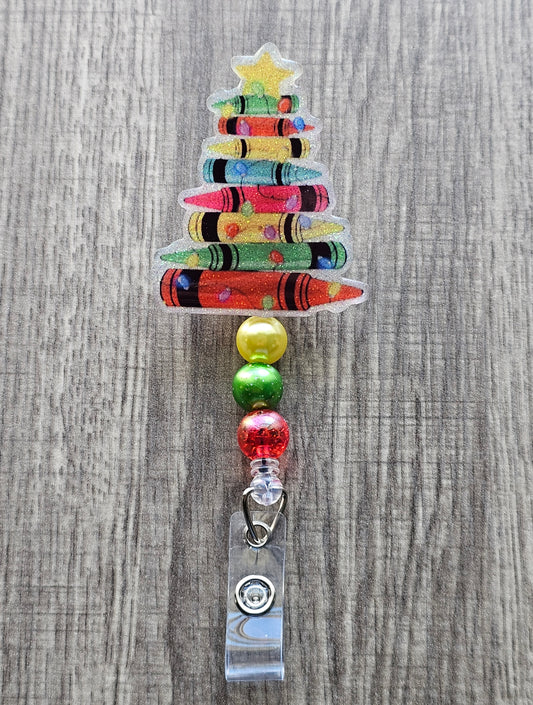 A badge reel featuring a a Christmas tree made from crayons along with a golden star featured at the top of the tree.