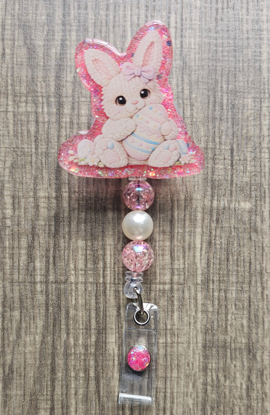 Handmade crochet white bunny badge reel holding a pink egg, surrounded by small felt flowers and eggs.