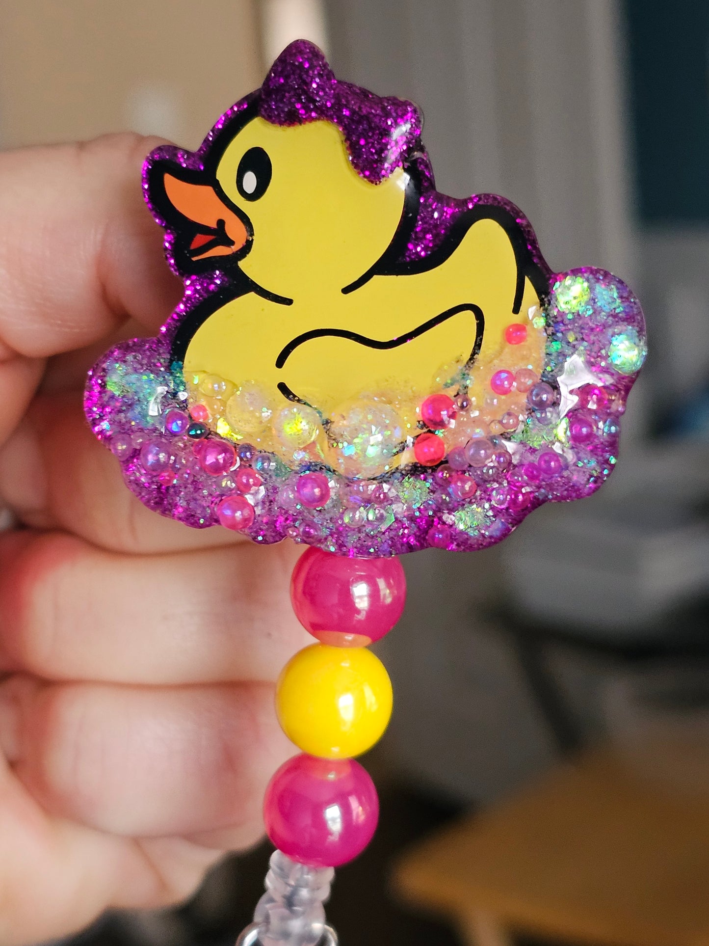 A badge reel featuring a cute rubber duck with a dark pink bow, surrounded by bubbles.