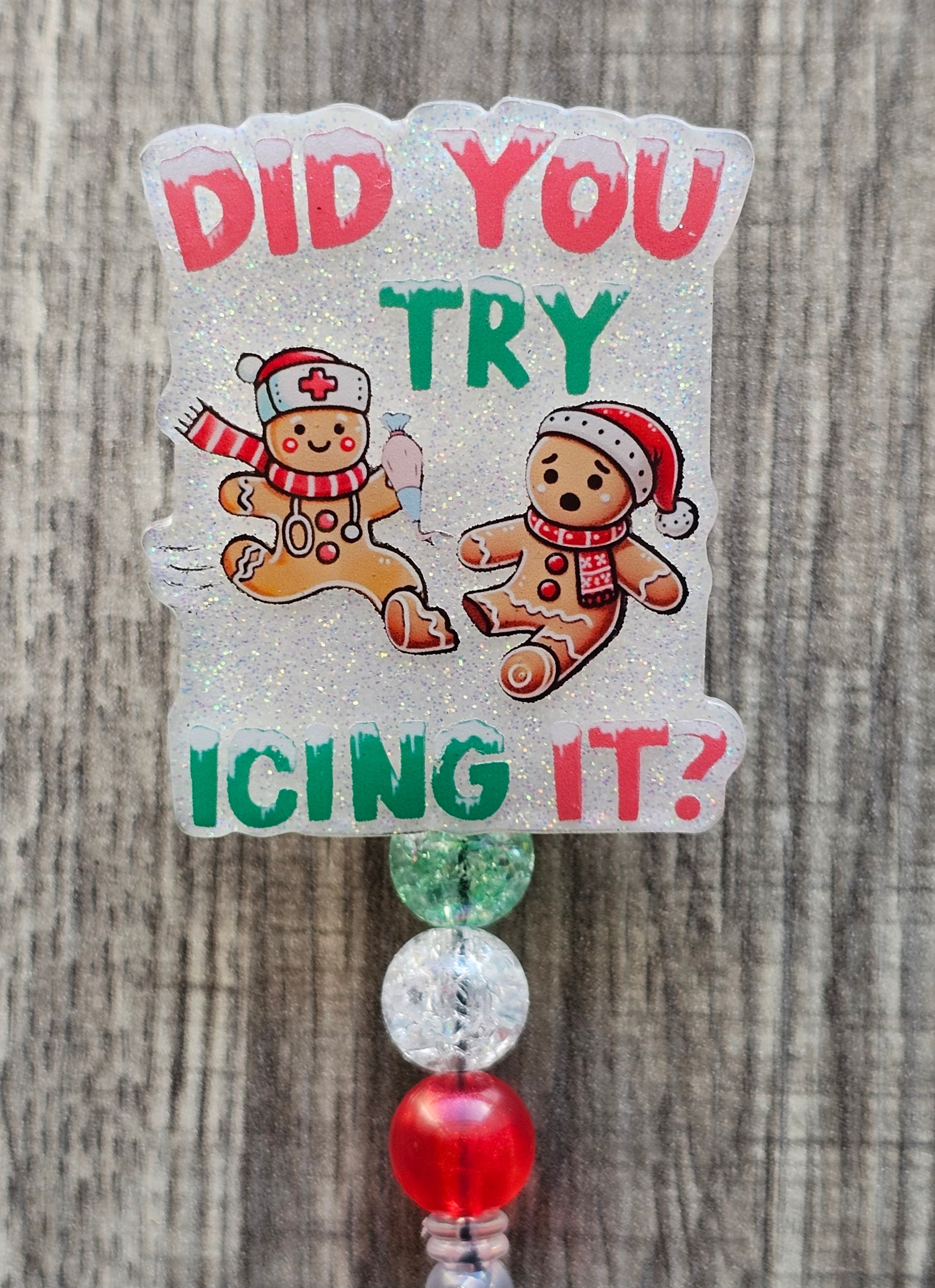 A Badge reel stating  Did You Try Icing It? while displaying a gingerbread man adorned with a nurse Christmas hat and stethoscope, while the other gingerbread man sits on the floor sad adorned with a Christmas hat and scarf along with a broken foot.