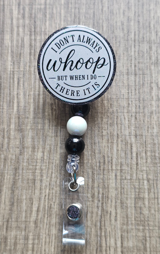 A retractable badge reel with a circular black and white printed top that reads 'I DON'T ALWAYS whoop BUT WHEN I DO THERE IT IS', shown on a light wood background. The reel is attached to black and white beads, a clear acrylic sleeve, and a silver lobster clasp.