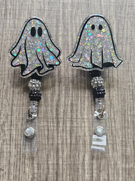A pair of silver glitter ghost-shaped badge reels. One ghost has wide eyes, the other has narrower eyes. Both are adorned with matching silver beads.
