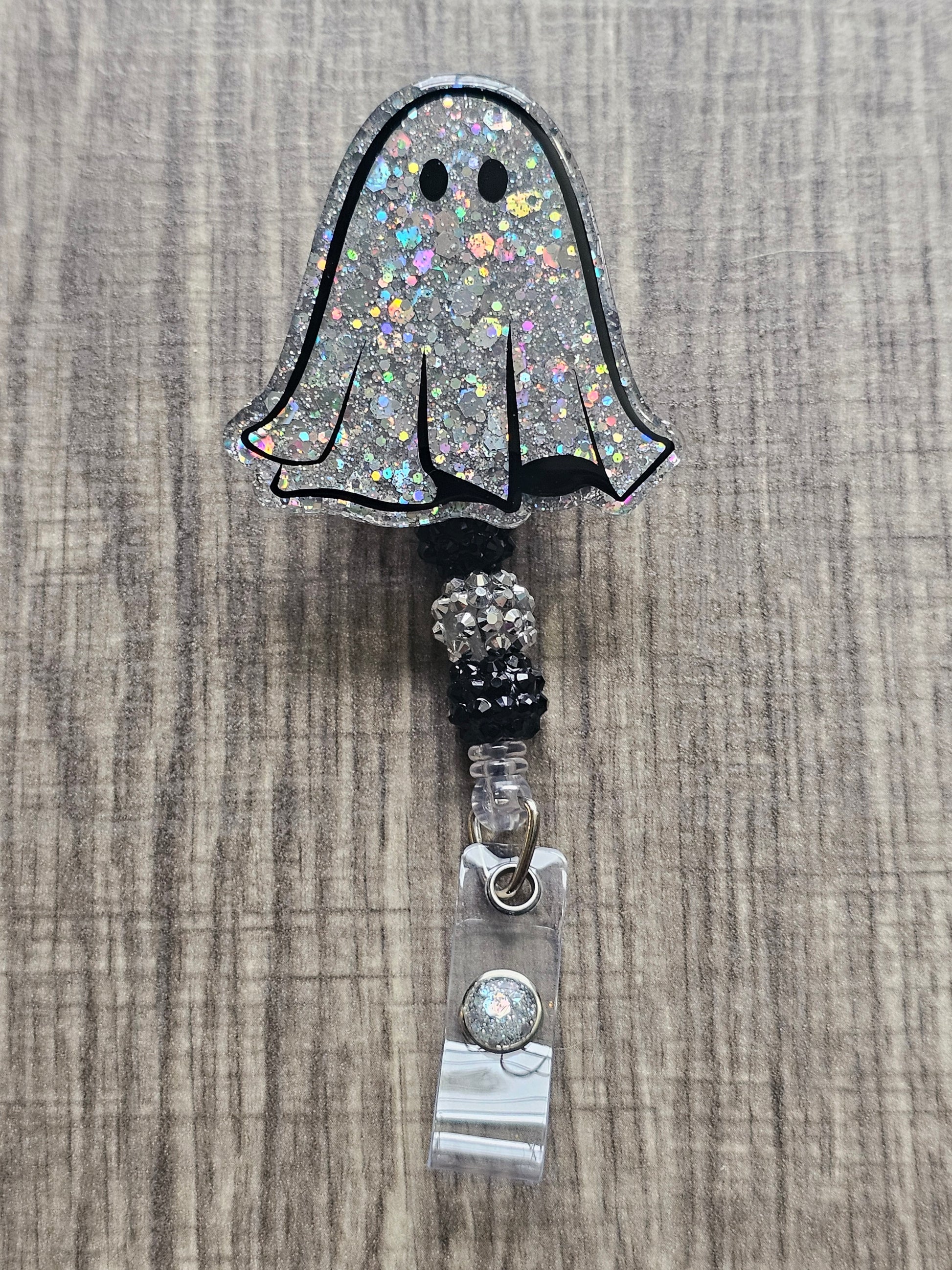 A pair of silver glitter ghost-shaped badge reels. One ghost has wide eyes, the other has narrower eyes. Both are adorned with matching silver beads.
