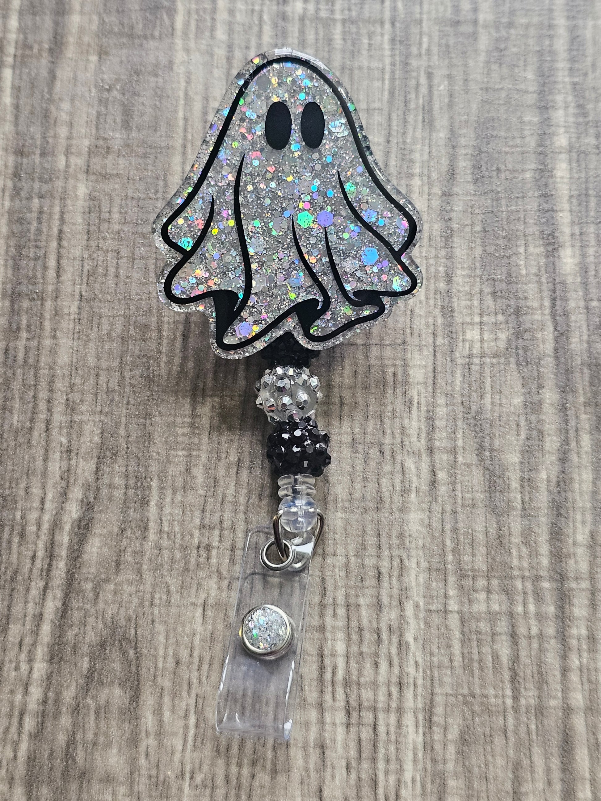 A pair of silver glitter ghost-shaped badge reels. One ghost has wide eyes, the other has narrower eyes. Both are adorned with matching silver beads.