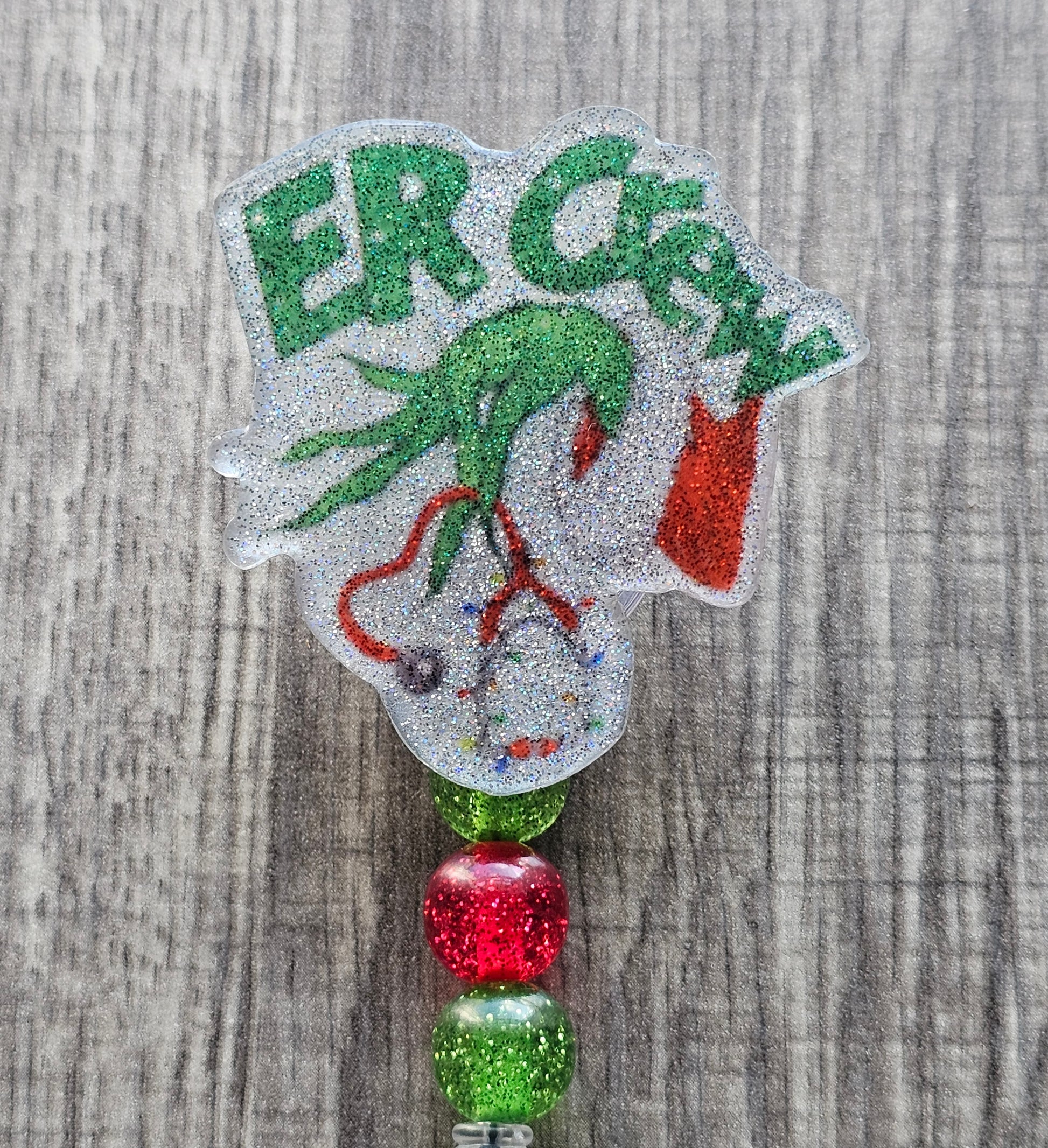 A badge reel featuring the hand of the grinch in a Christmas Sweater holding a festive themed Stethoscope with the words ER Crew.  