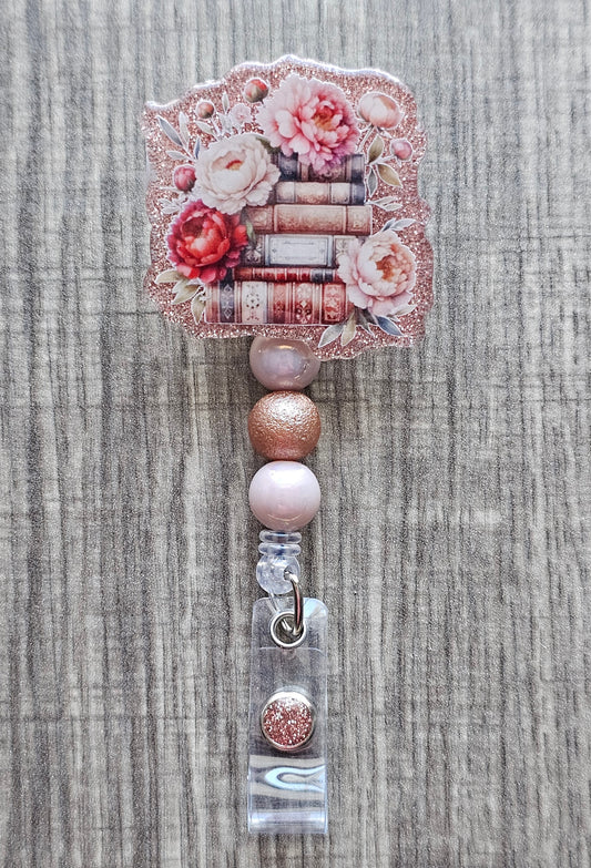 Stack of books badge reel with floral decorations on a pink acrylic background.