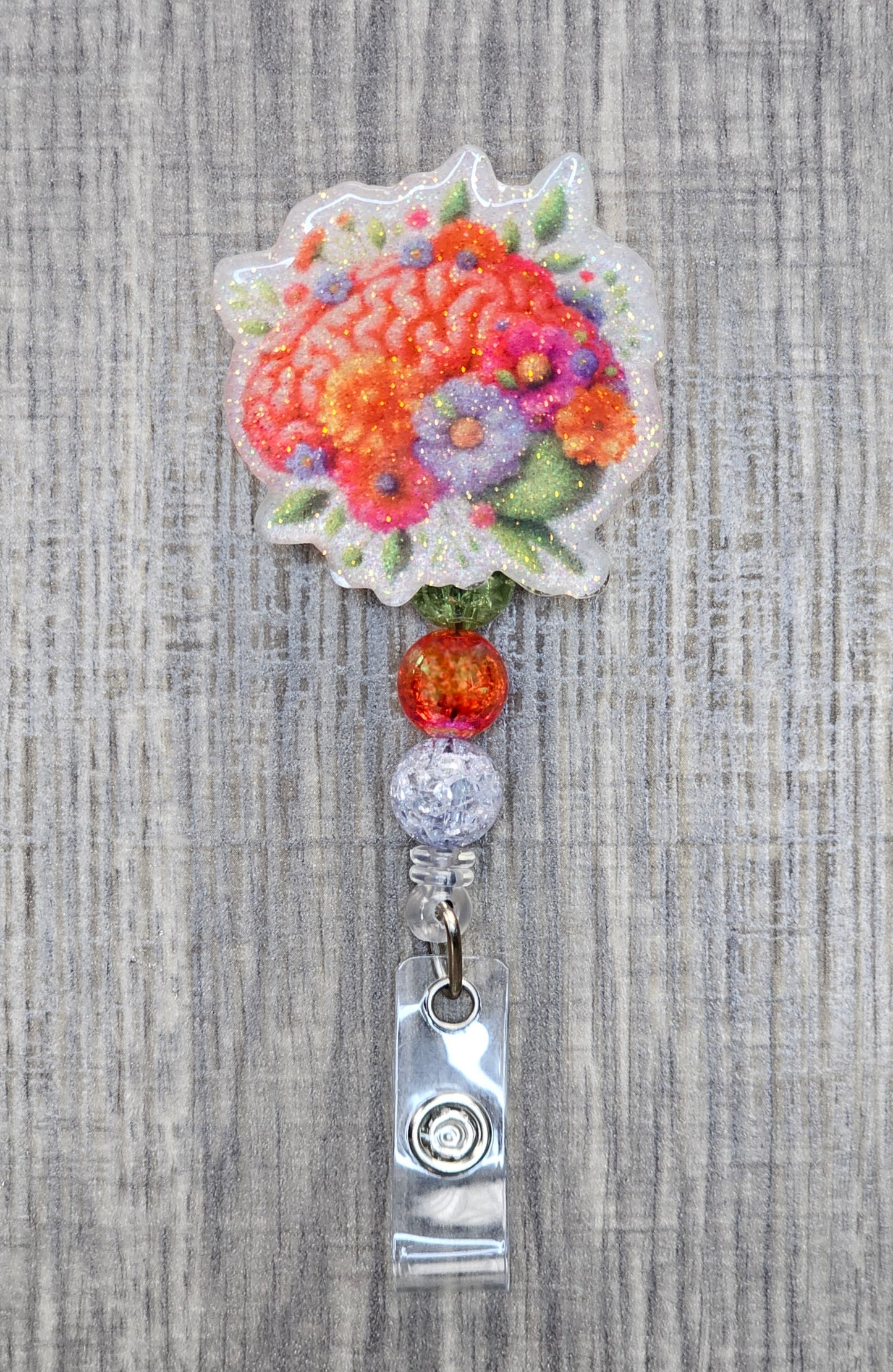 A colorful Brain graphic badge reel with flowers and leaves surrounding it, with beads.