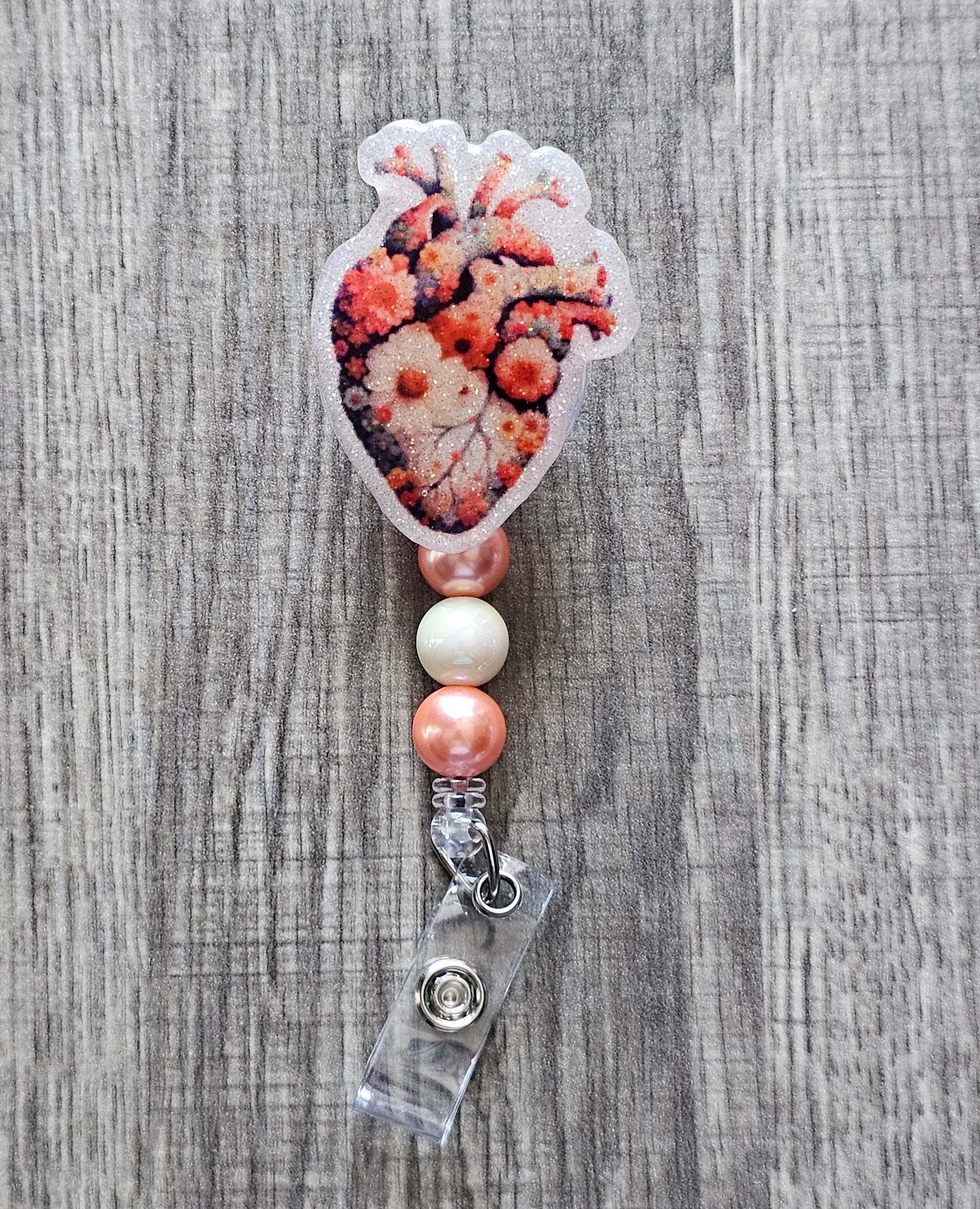 An elegant heart-shaped badge reel adorned with flowers all around. A beautiful, retractable accessory for compassionate professionals.