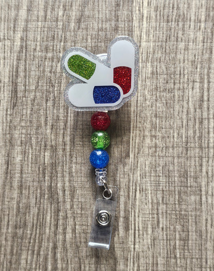 Badge reel shaped like 3 glitter pills: green, red, and blue.