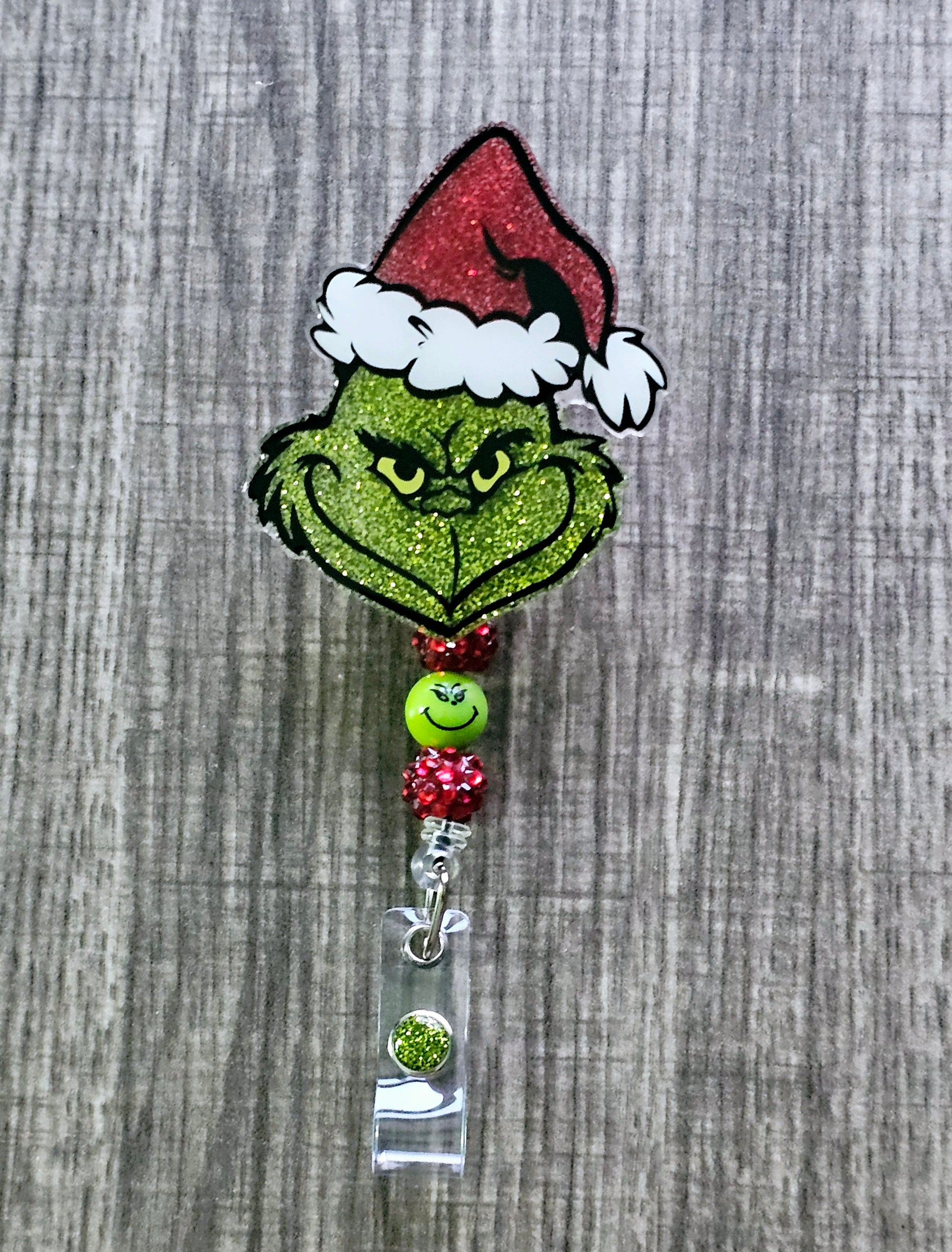 A badge reel featuring the face of the grinch grinning while wearing a Christmas hat 