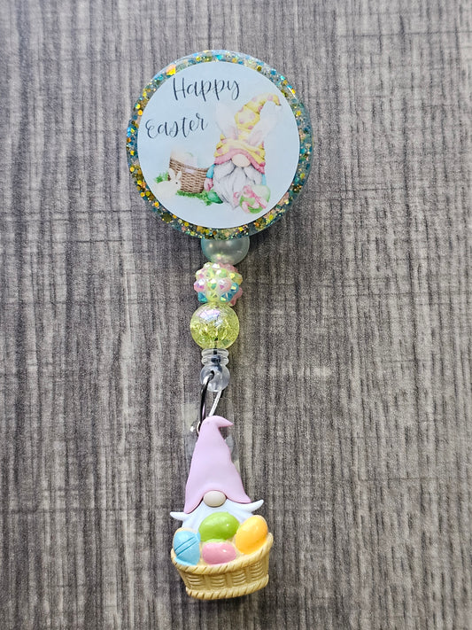 A badge reel stating happy easter displaying a gnome with bunny ears sitting with a picnic basket along a bunny.