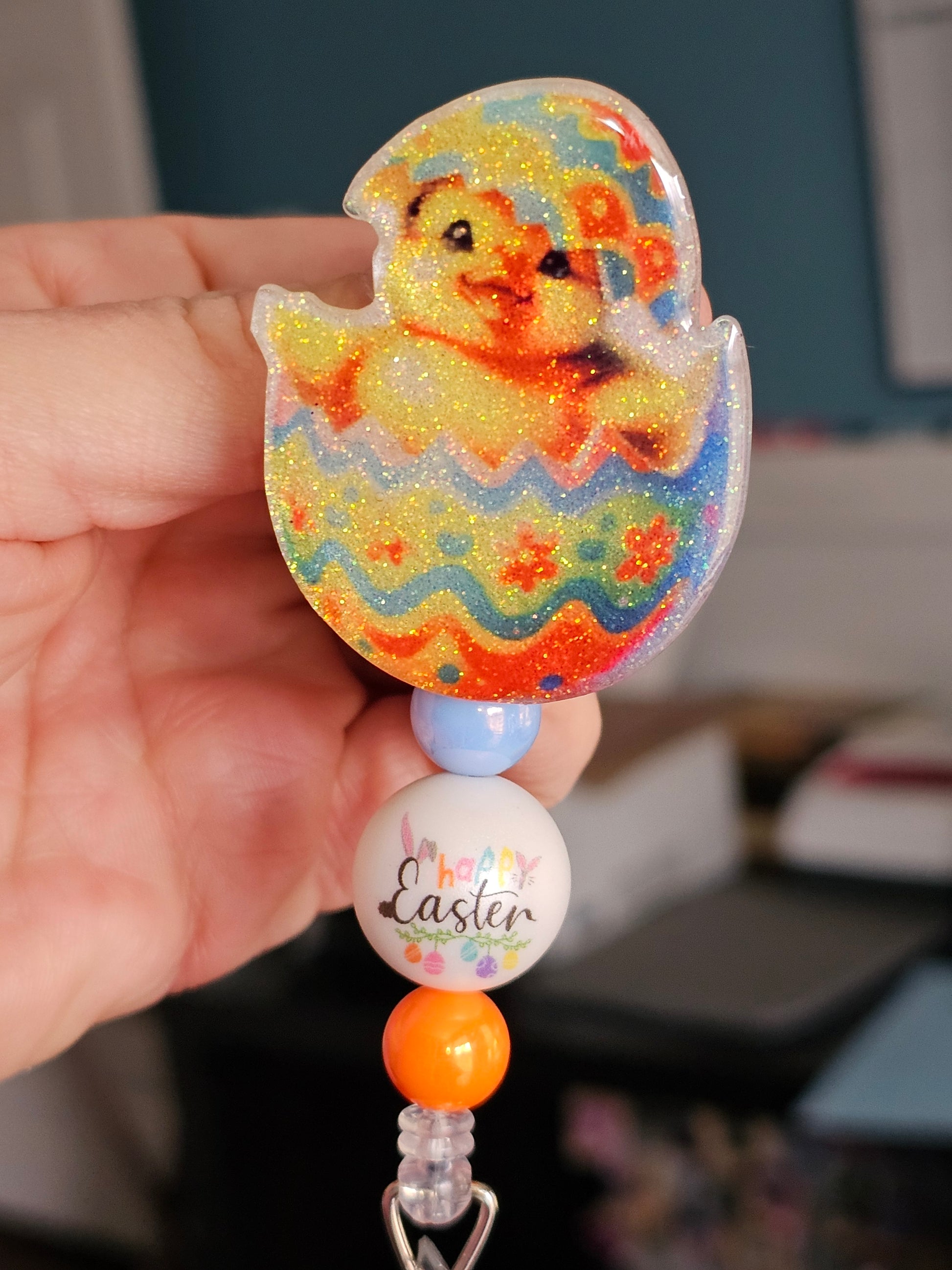 A badge reel featuring a baby duck hatching from a colorful Easter egg, available in two variants.