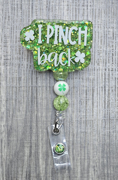 Retractable St. Patrick's Day badge reel with "I Pinch Back" text, featuring green beads and a central four-leaf clover bead.