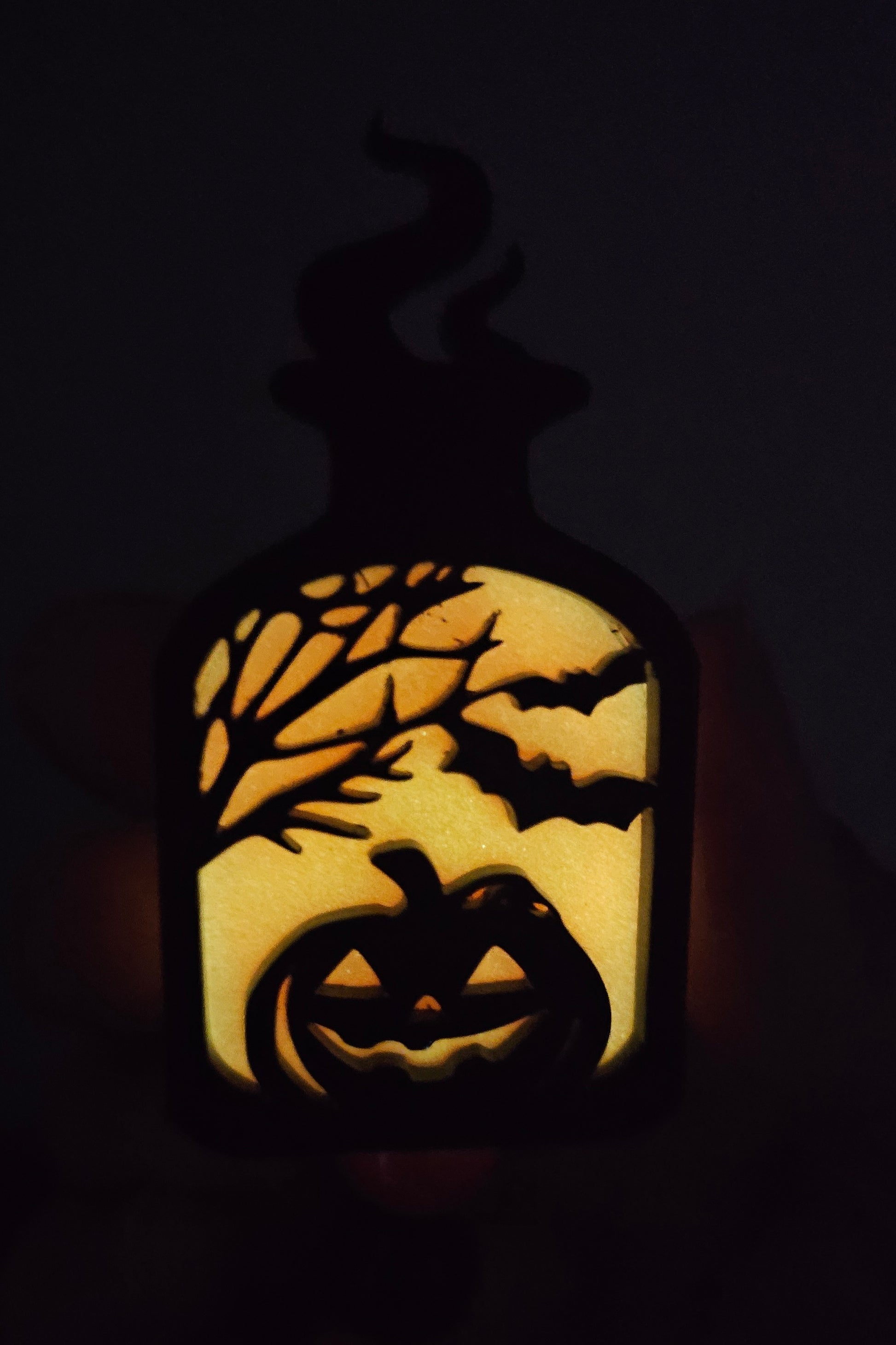Orange glow-in-the-dark potion bottle-shaped badge reel with an eerily smiling jack-o-lantern surrounded by trees and bats, with matching glow-in-the-dark decorative beads.