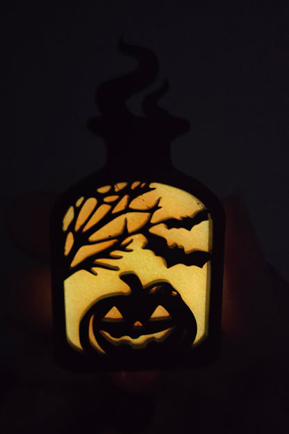 Orange glow-in-the-dark potion bottle-shaped badge reel with an eerily smiling jack-o-lantern surrounded by trees and bats, with matching glow-in-the-dark decorative beads.