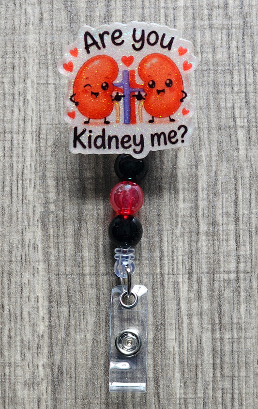 A badge reel with a medical humor theme, featuring two cartoon kidney characters with a heart line between them, and the phrase 'Are you Kidney me?' printed at the top.