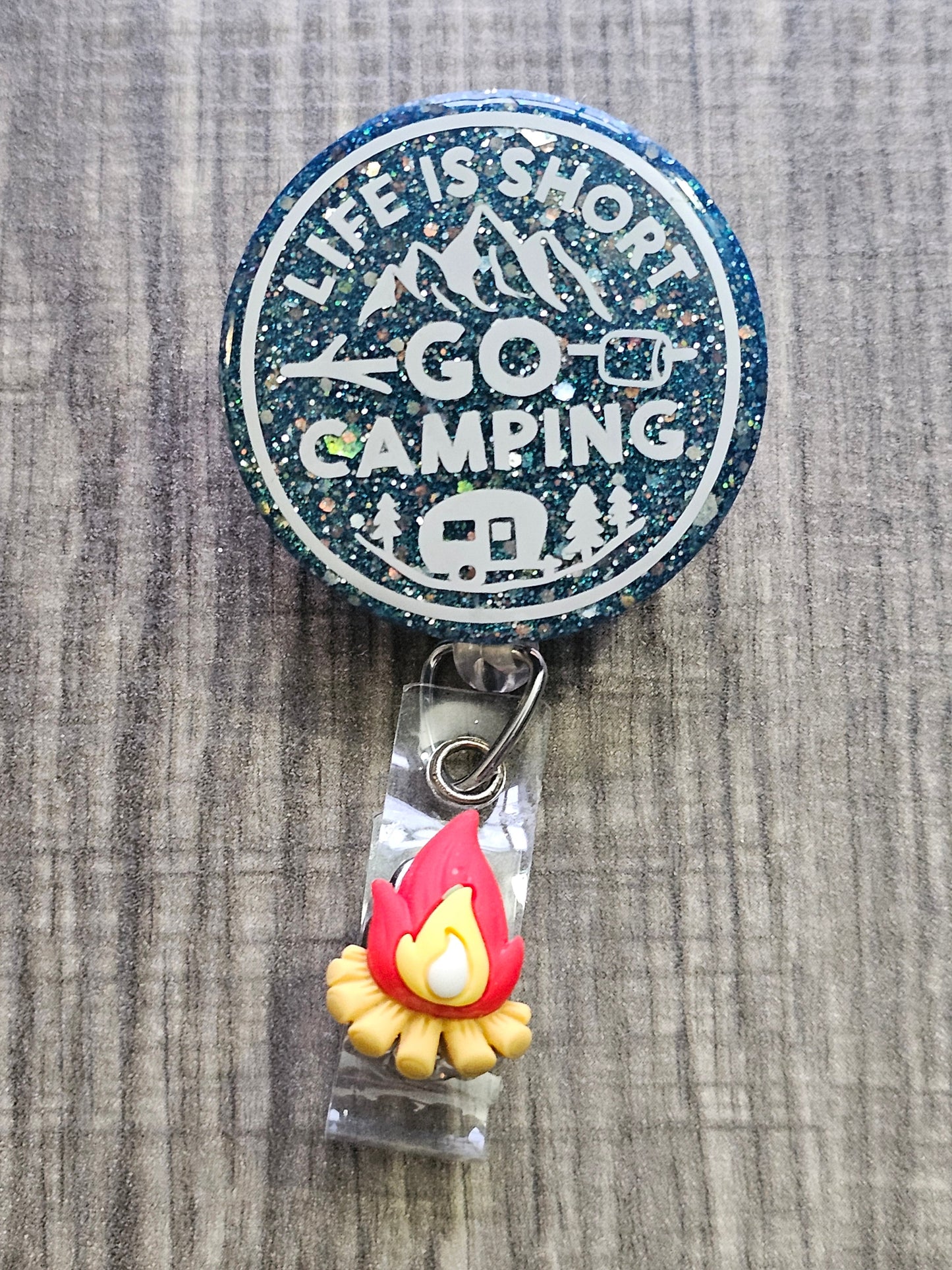  A Badge Reel featuring the statement life is short go camping with a peacock green background and camping décor