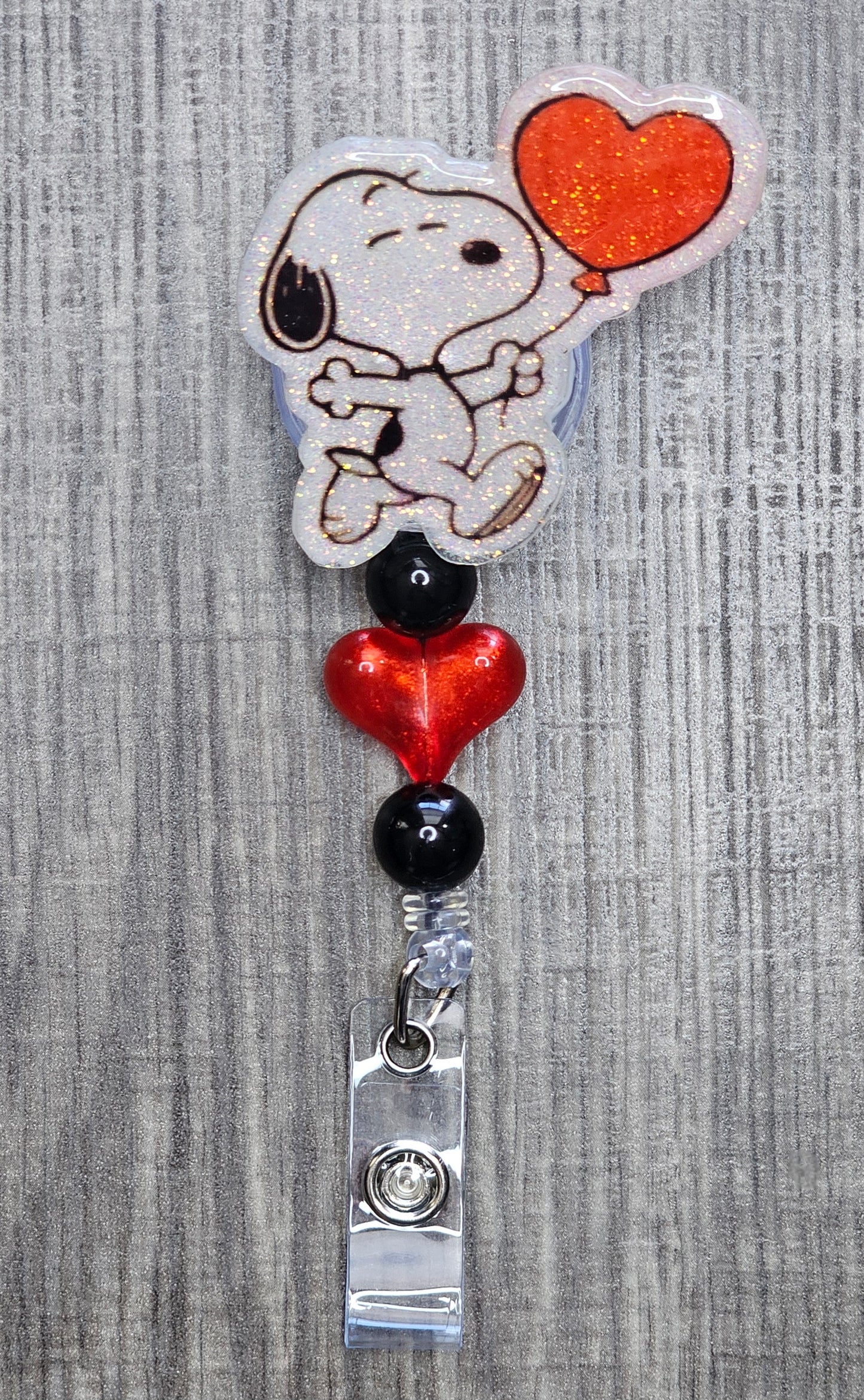 Snoopy holding a heart shaped balloon badge reel with red and black heart beads.