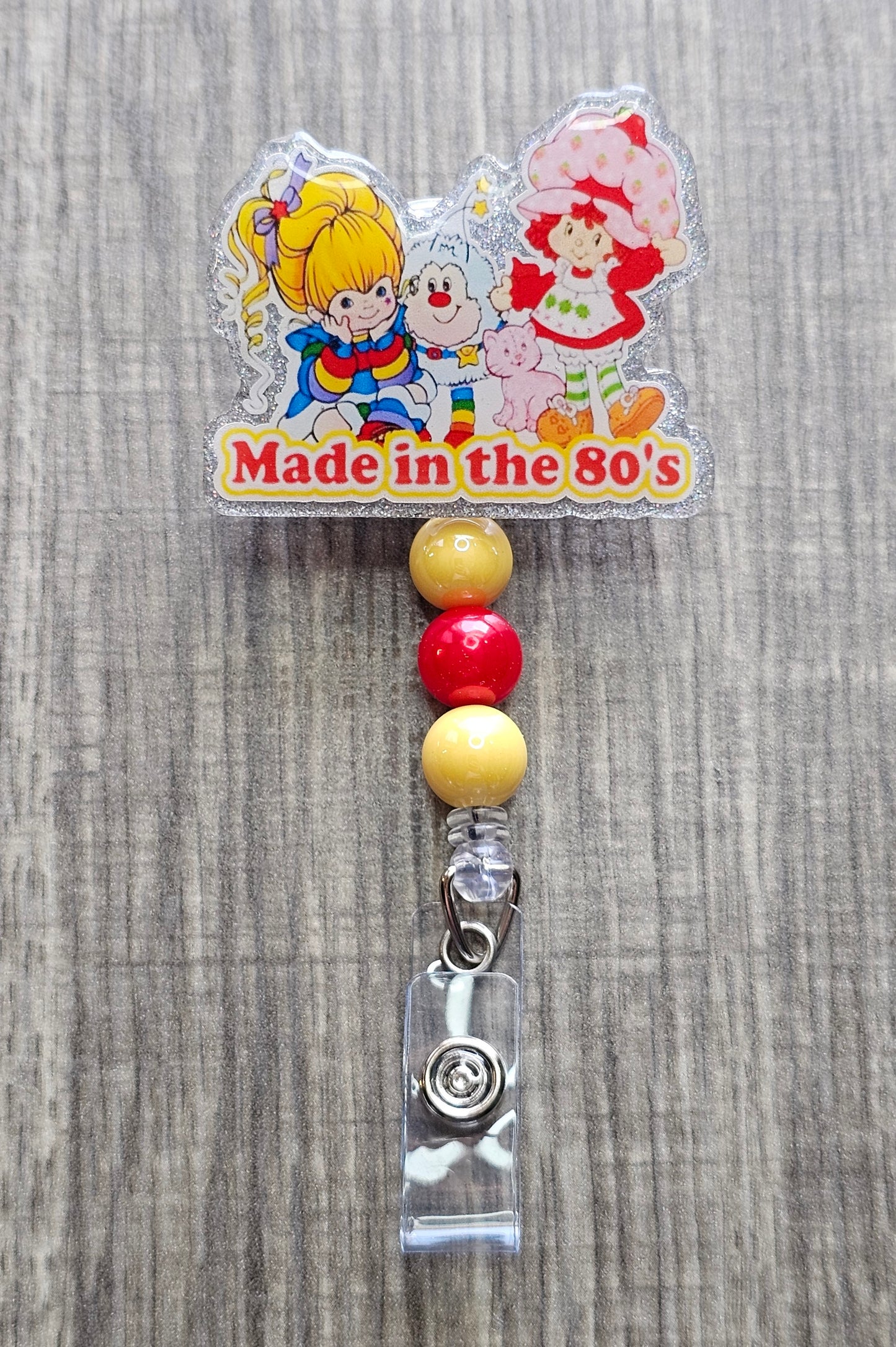 Retro 80s cartoon character badge reel featuring Strawberry Shortcake and a Rainbow Brite design.
