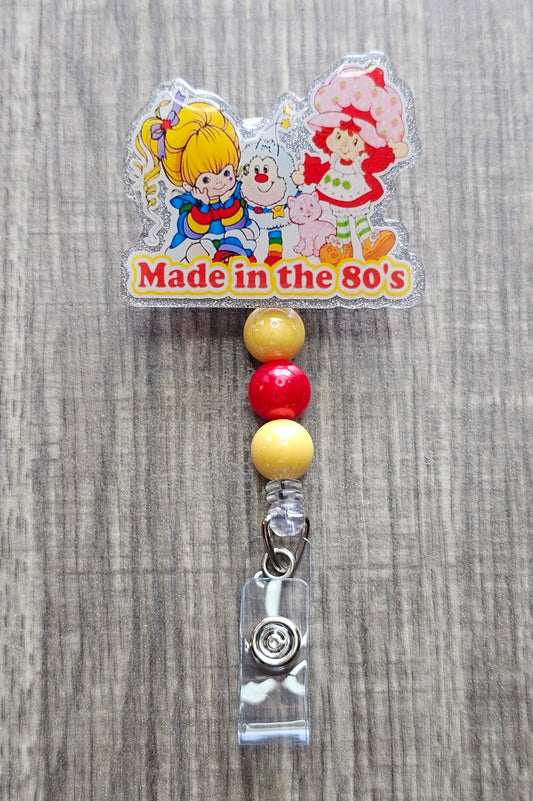 Retro 80s cartoon character badge reel featuring Strawberry Shortcake and a Rainbow Brite design.