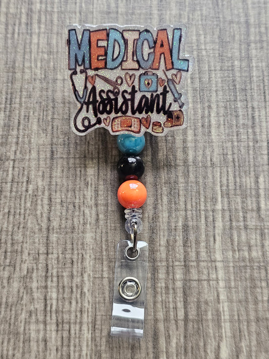 White glitter acrylic badge reel with "Medical Assistant" text, featuring a stethoscope, scissors, first aid kit, syringe, hearts, and medicine, with creatively matching decorative beads.