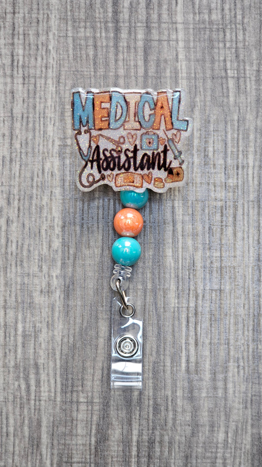 White glitter acrylic badge reel with "Medical Assistant" text, featuring a stethoscope, scissors, first aid kit, syringe, hearts, and medicine, with creatively matching decorative beads.