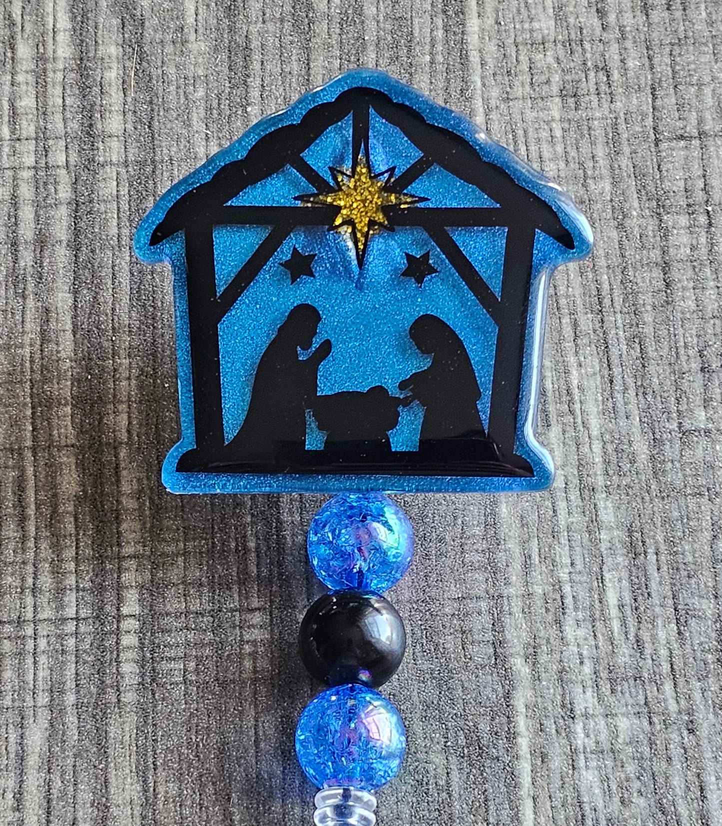 A badge reel featuring  a manger with Joseph and Mary kneeling Infront of the baby Christ. On top of the manger displaying the northern star that guided them to the birthplace of Christ