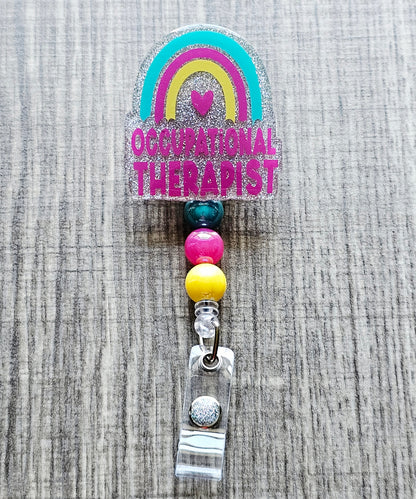 Glitter occupational therapist badge reel with a rainbow and heart design.
