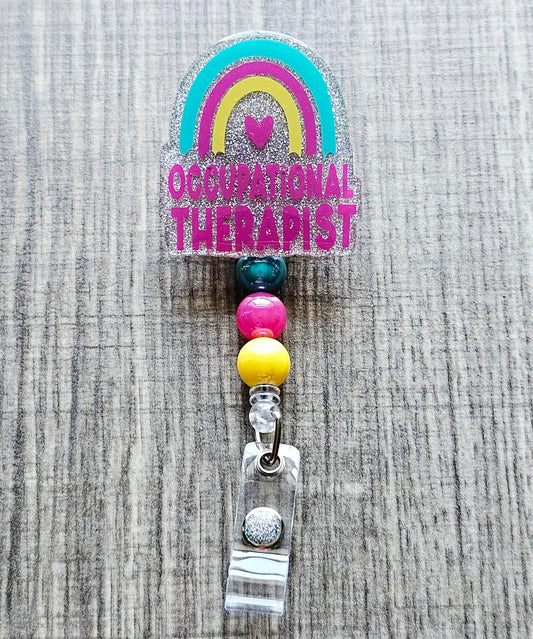 Glitter occupational therapist badge reel with a rainbow and heart design.