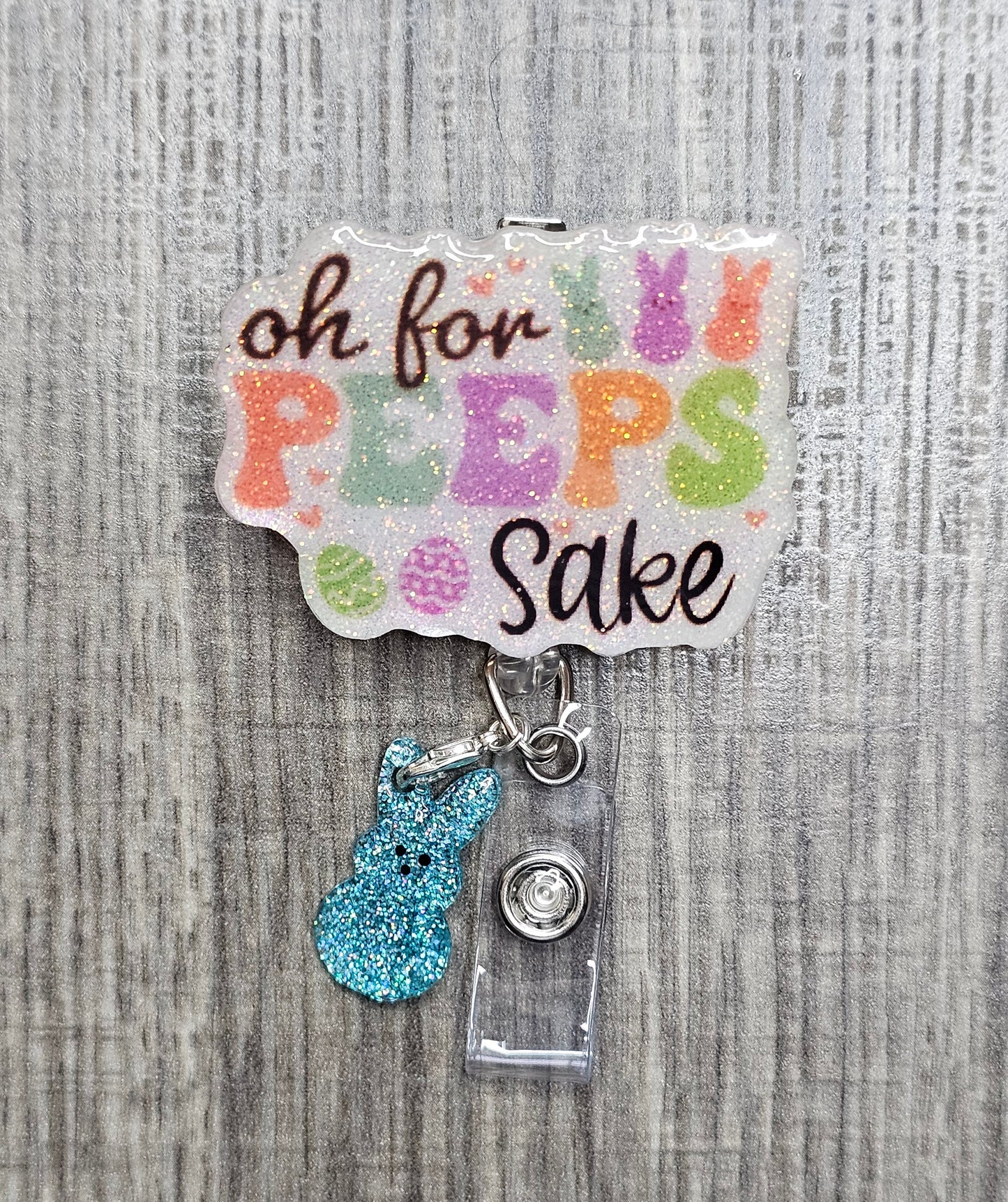 An Easter-themed badge reel with "Oh For Peeps Sake" text and a blue glittery bunny clip attachment.
