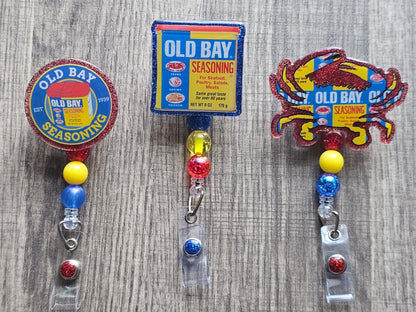 3 Different Badge reels ;one shaped like the classic Old Bay container, another featuring a crab with the Old Bay logo, and a circular design that proudly displays the seasoning's original creation date.