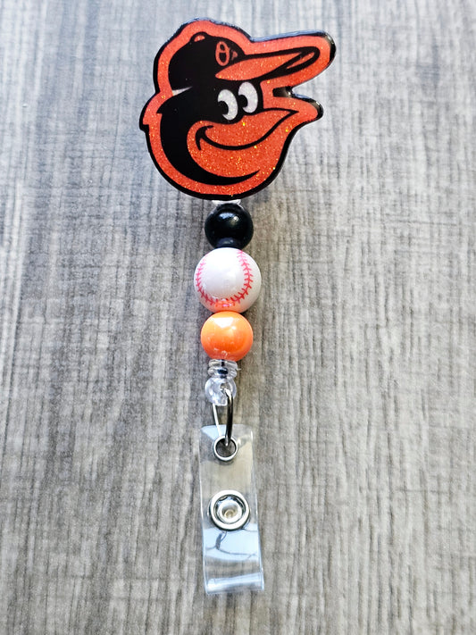 Handcrafted Orioles-inspired bird mascot badge reel with baseball beads  glitter finish.
