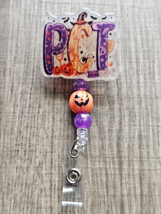 White glitter acrylic badge reel with Halloween-themed "PCT" letters, featuring bats, jack-o-lanterns, a Halloween syringe, and a witch's hat on the 'C', with matching beads and a jack-o-lantern bead.