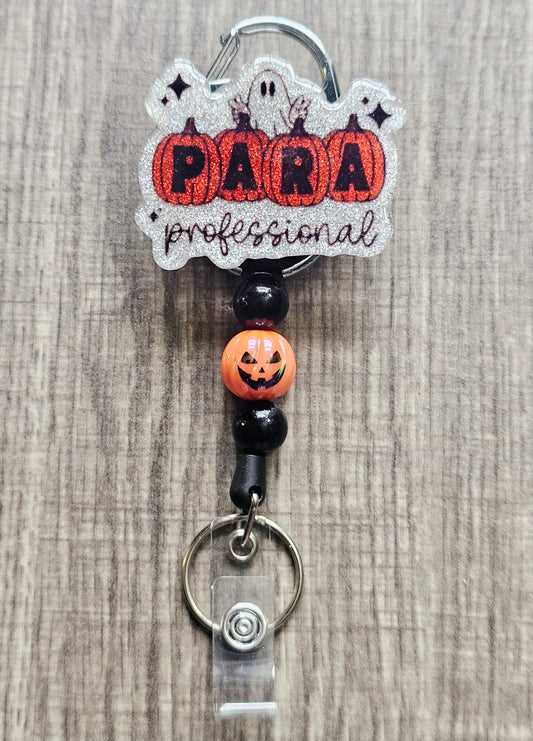 White glitter acrylic badge reel with pumpkins spelling "Para," "Professional" written below, a ghost behind the pumpkins, and matching beads with a central jack-o-lantern bead.