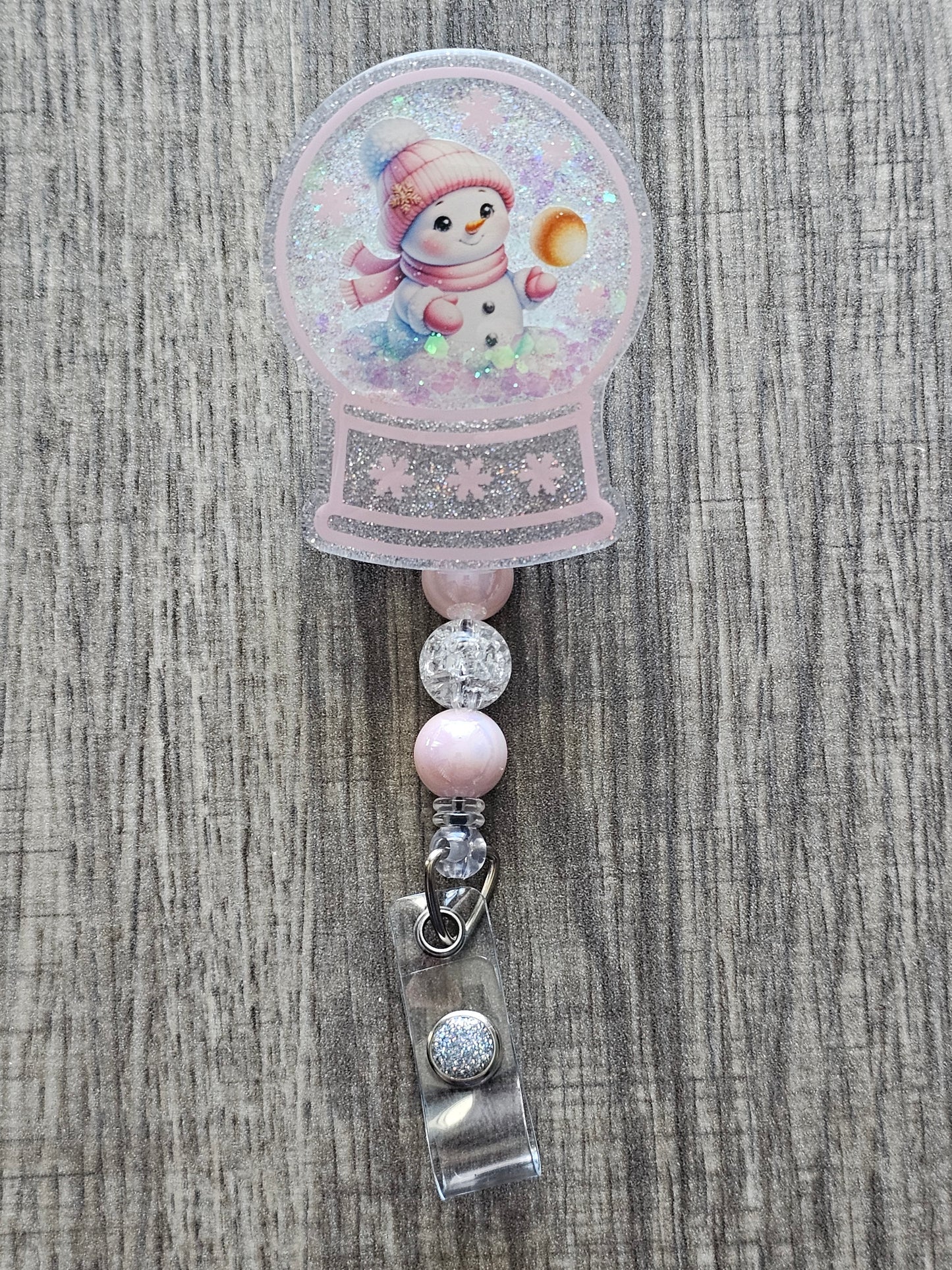 A badge reel with a snow globe design featuring an adorable snowman with a golden snowball