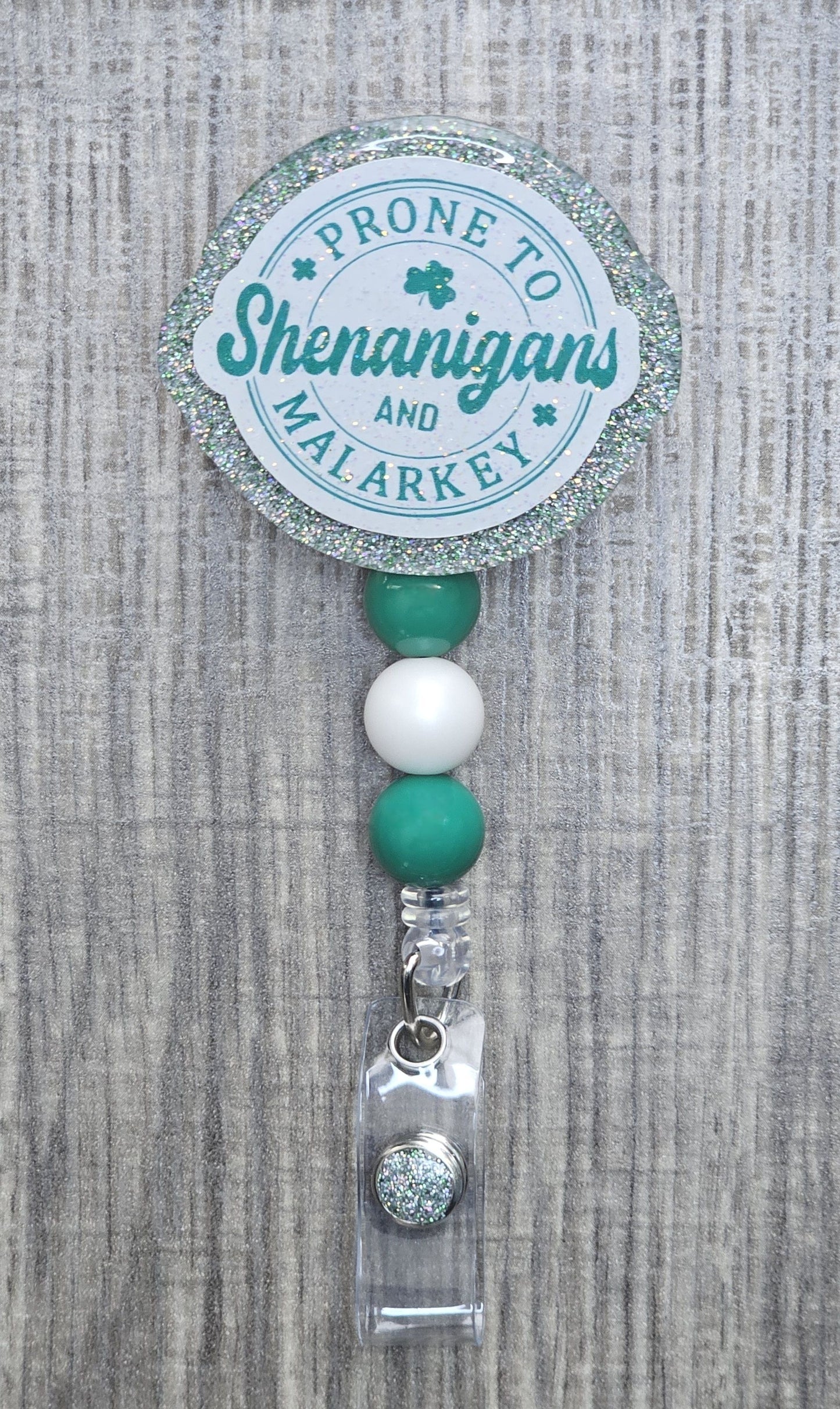 Round retractable badge reel with green text reading "Prone to Shenanigans and Malarkey" for St. Patrick's Day.
