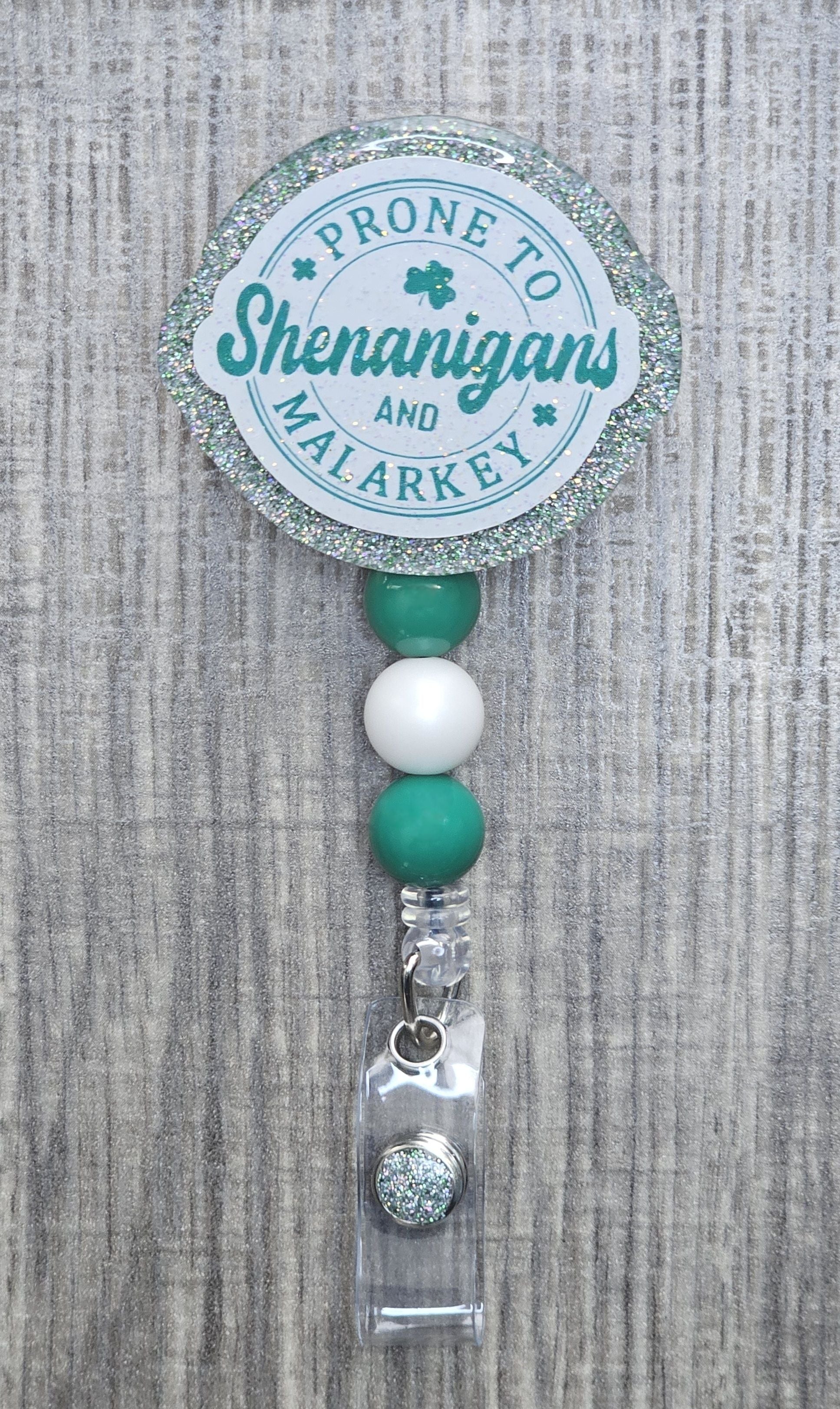 Round retractable badge reel with green text reading "Prone to Shenanigans and Malarkey" for St. Patrick's Day.