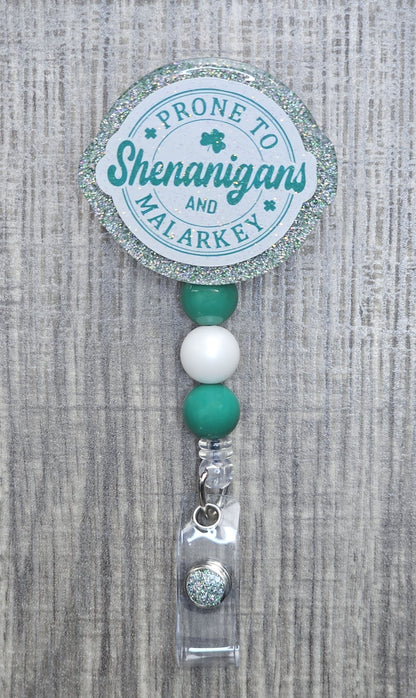 Round retractable badge reel with green text reading "Prone to Shenanigans and Malarkey" for St. Patrick's Day.