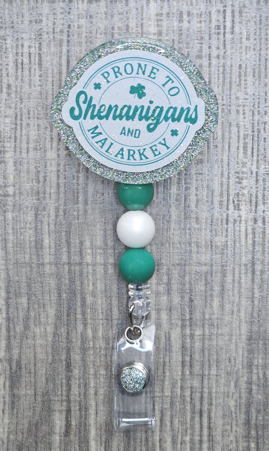Round retractable badge reel with green text reading "Prone to Shenanigans and Malarkey" for St. Patrick's Day.