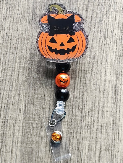 A badge reel featuring a cat popping its head out of a jack-o-lantern