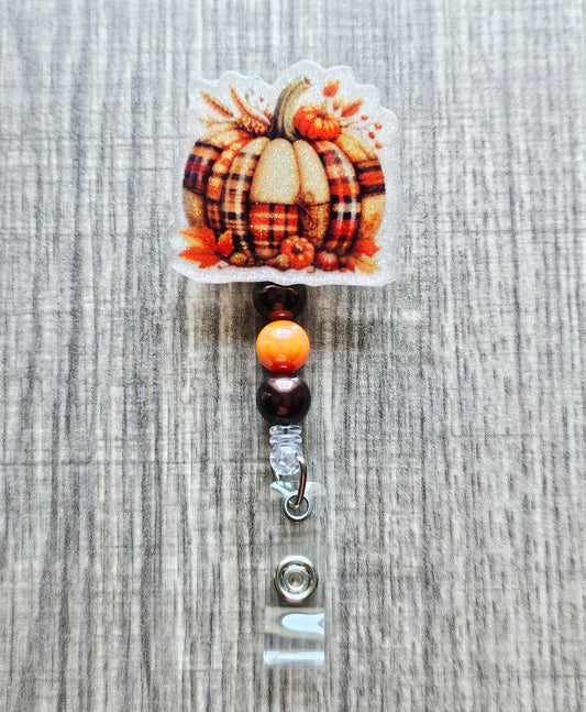 A retractable badge reel featuring a festive patchwork pumpkin design for the fall season.