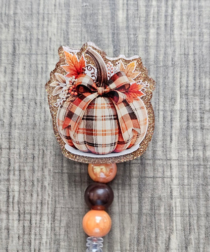 A retractable badge reel featuring a festive patchwork pumpkin design for the fall season.