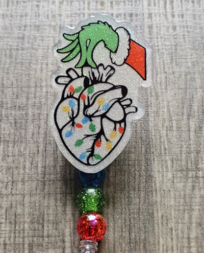 A badge reel displaying a well known mischievous grinch hand wearing a cozy Christmas sweater, delicately holding a heart adorned with twinkling Christmas lights.